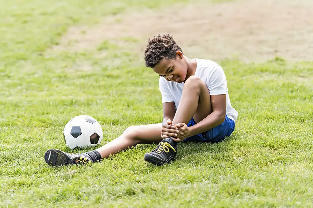 young boy holding ankle on soccer field