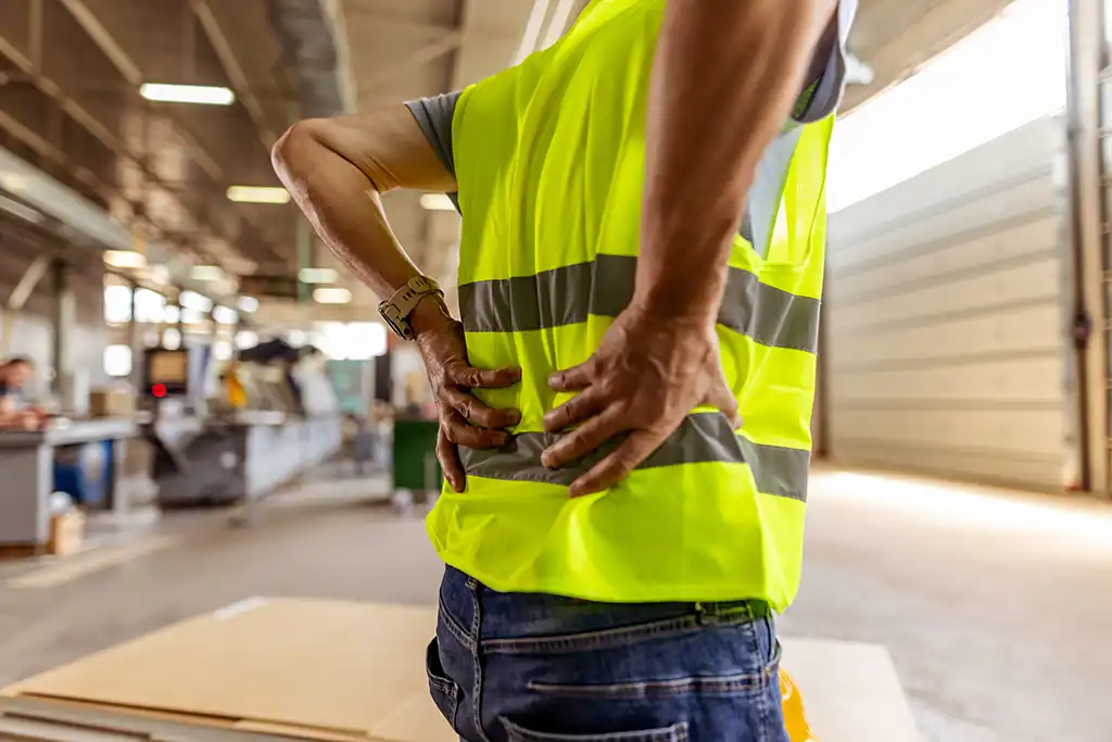 man on construction site holding his bad back